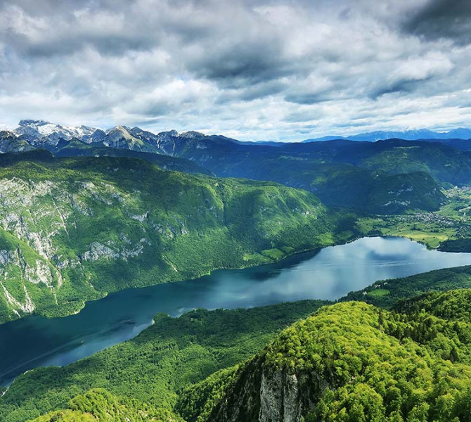 Panoramic view of Lake Bohinj surrounded by green forests and mountains in the background.