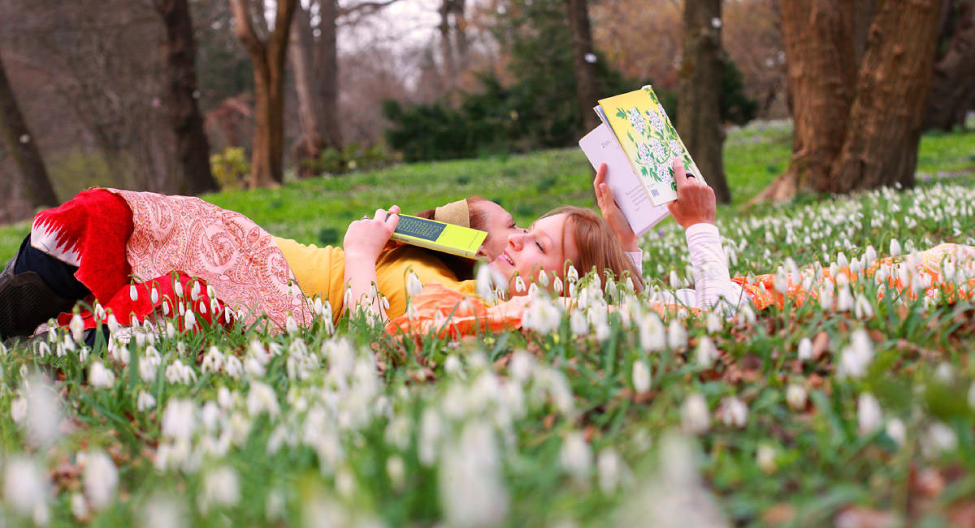 Dekleti ležita med zvončki v Botaničnem vrtu in bereta knjigo.