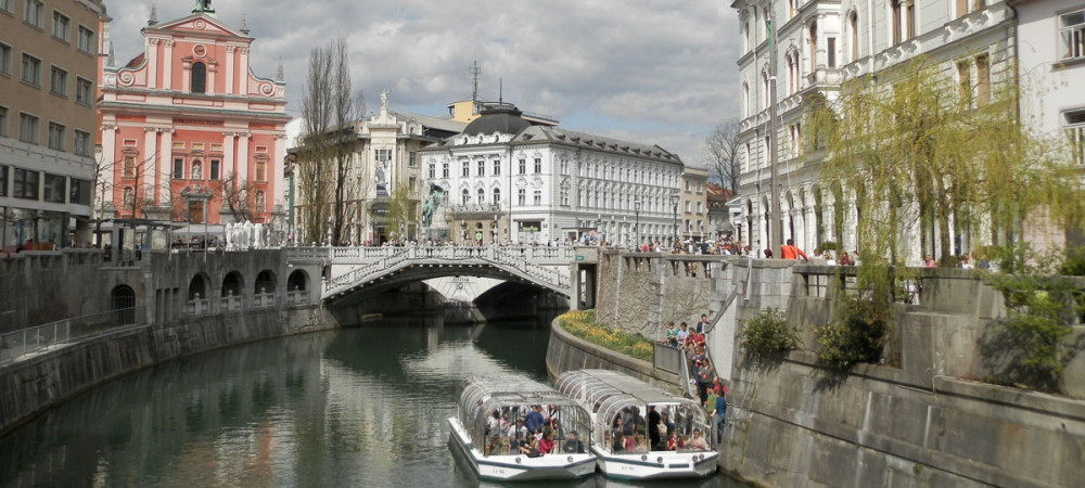 Razgled iz mosta na turistični ladjici na Ljubljanici. V ozadju Tromostovje in Prešernov trg.