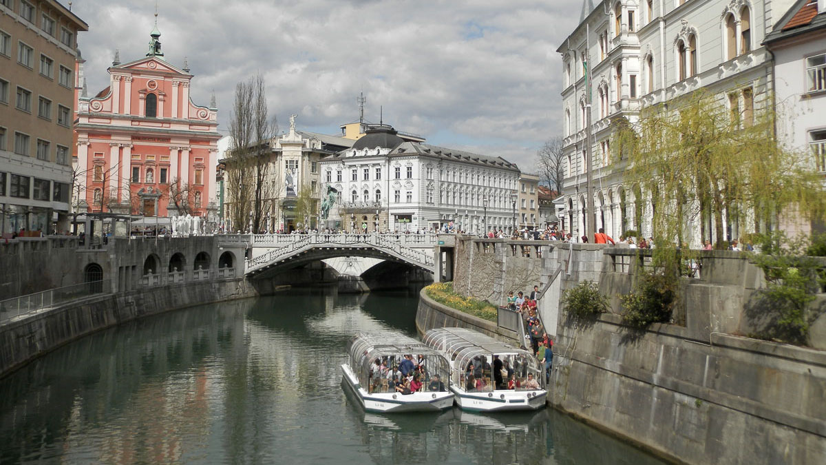 Razgled iz mosta na turistični ladjici na Ljubljanici. V ozadju Tromostovje in Prešernov trg.