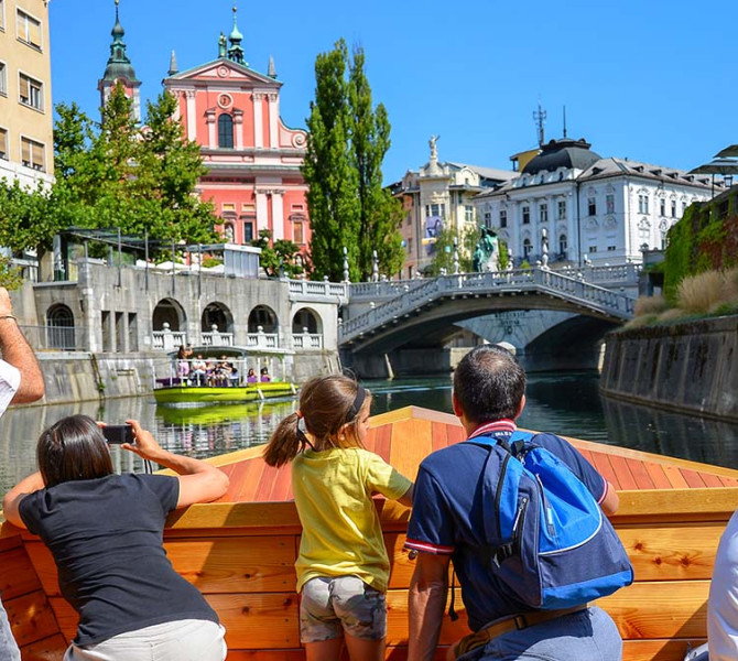 View from a boat sailing along the river through the city, where people are observing the surroundings and taking photos.