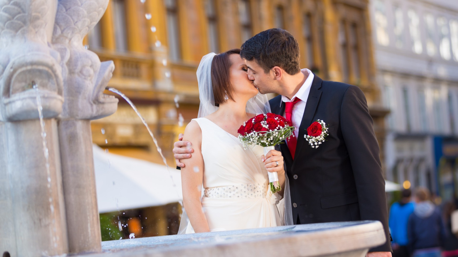 Mladoporočenca se poljubljata pred vodnjakom na Gornjem trgu.
