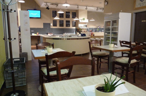 Notranjost restavracije z mizami in stoli, ter šankom v ozadju. 