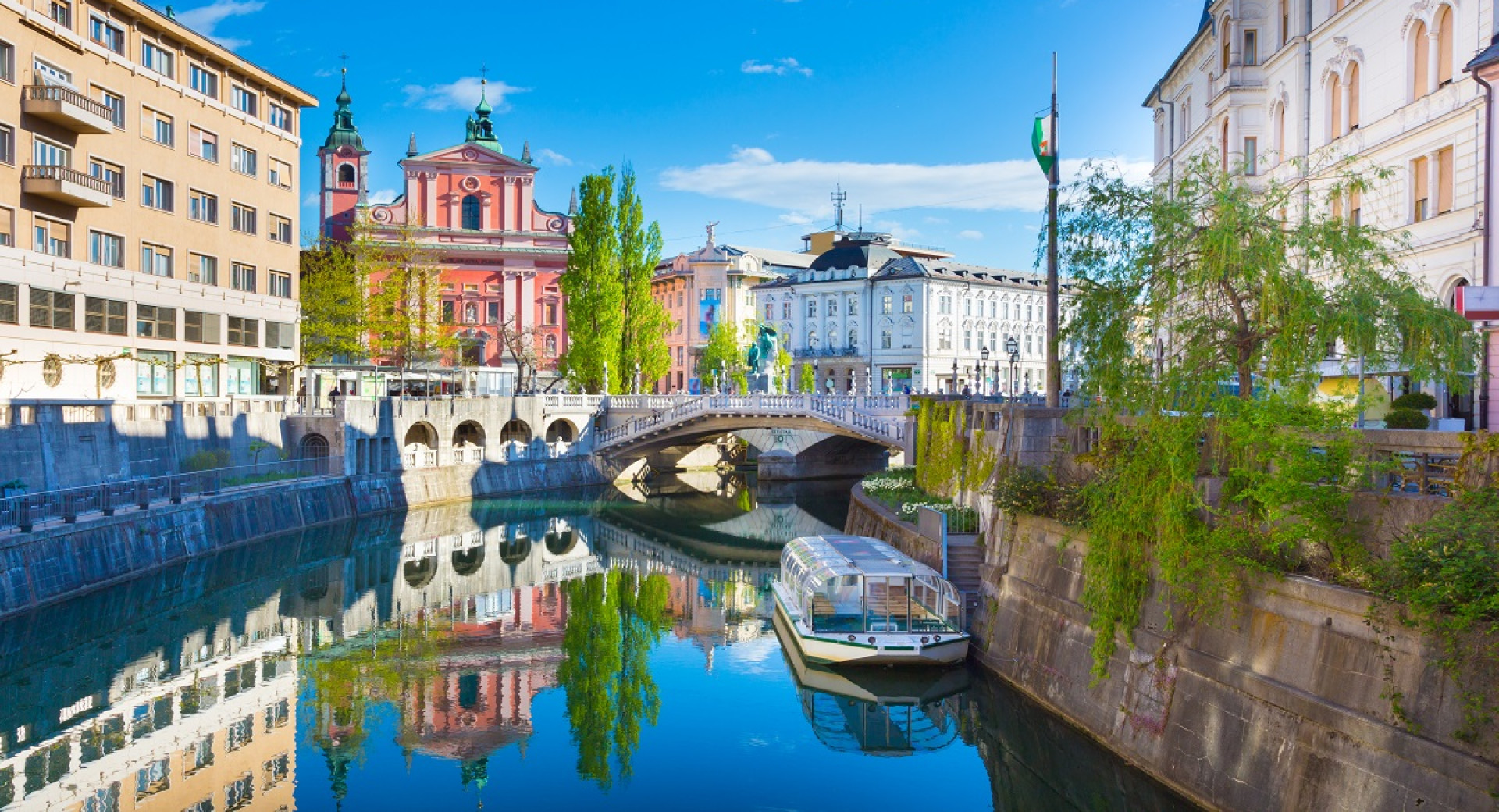 View from the bridge of the Ljubljanica River and a boat, with Preseren Square in the background.