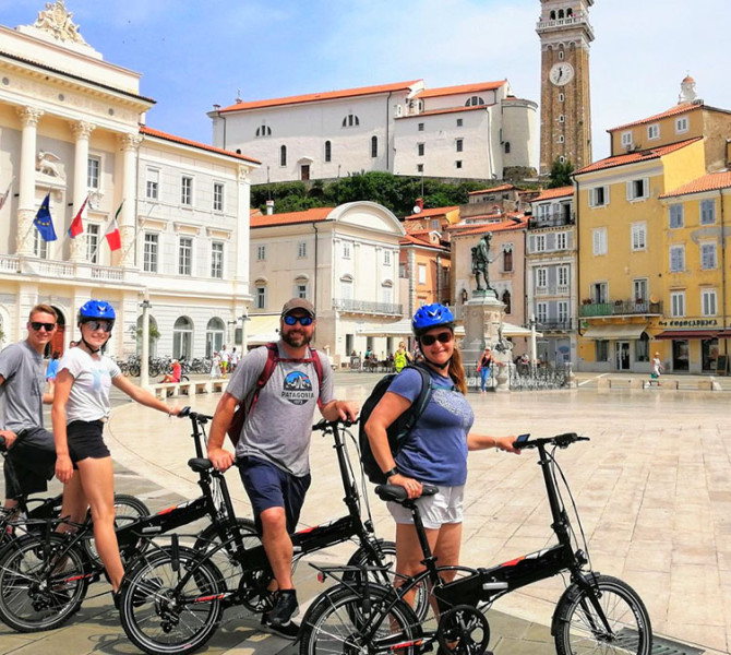 A group of four cyclists in Tartini Square, with the Town Hall and buildings in the background.
