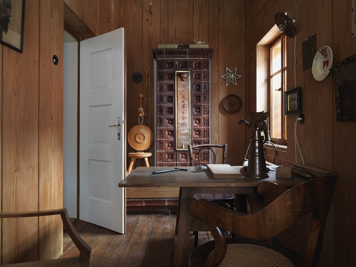 Odprta vrata v Plečnikovo sobo, lesena miza in stol ter drobni predmeti.