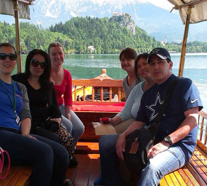 Obiskovalci na pletni, na Blejskem jezeru. V ozadju Blejski grad.