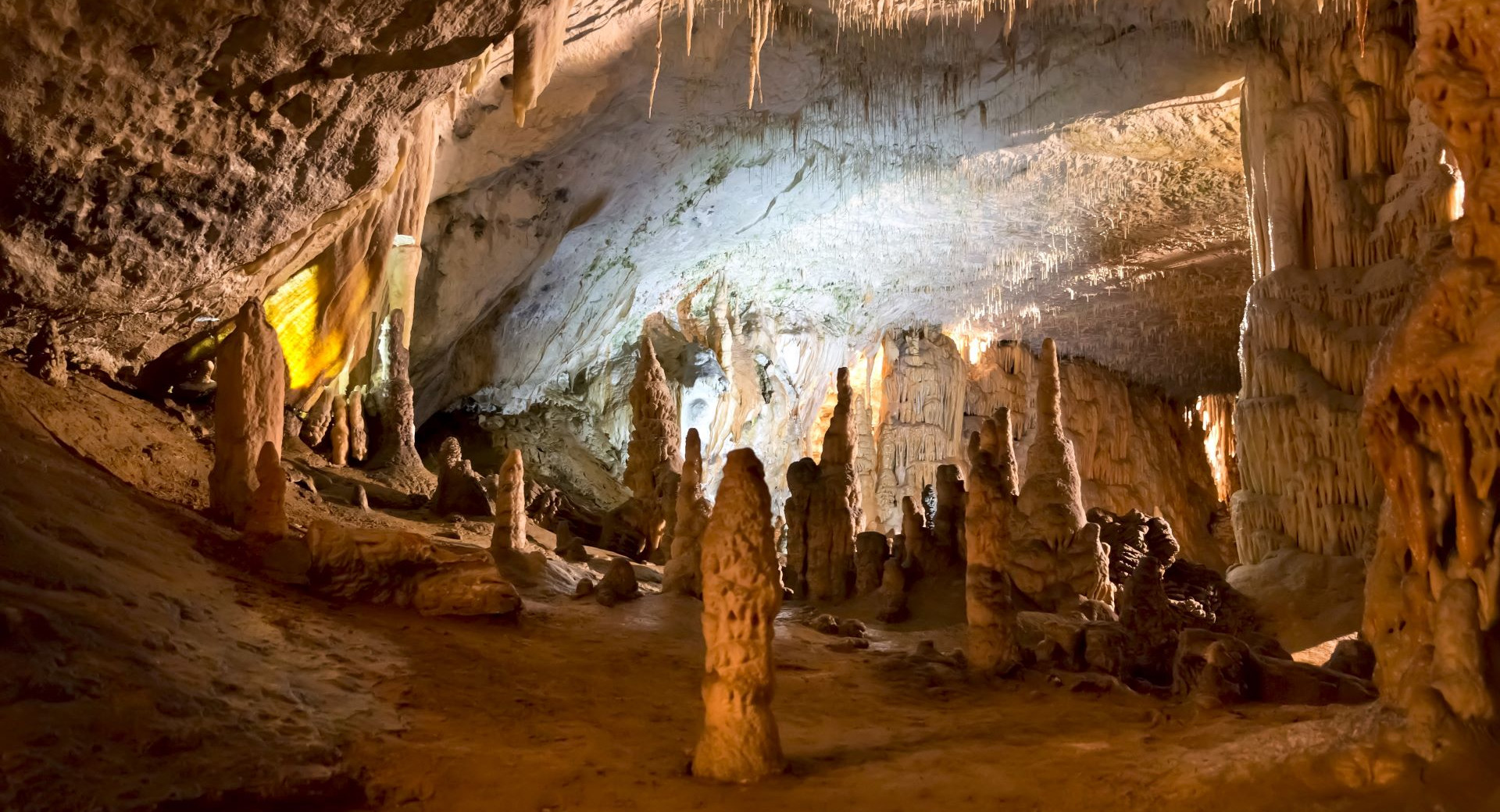 Notranjost Postojnske jame s cudovitimi kapniki, stalaktiti in stalagmiti, osvetljenimi v toplih barvah, ki ustvarjajo carobno podzemno vzdusje.