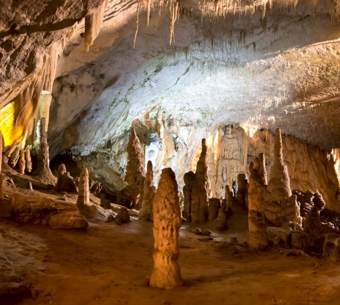 Innenraum der Postojna-Höhle mit wunderschönen Stalaktiten und Stalagmiten, die in warmen Farben beleuchtet sind und eine magische unterirdische Atmosphäre schaffen.