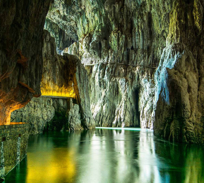 Interior of the Skocjan Caves with towering limestone walls, an underground river, and a lit pathway along the rock face.