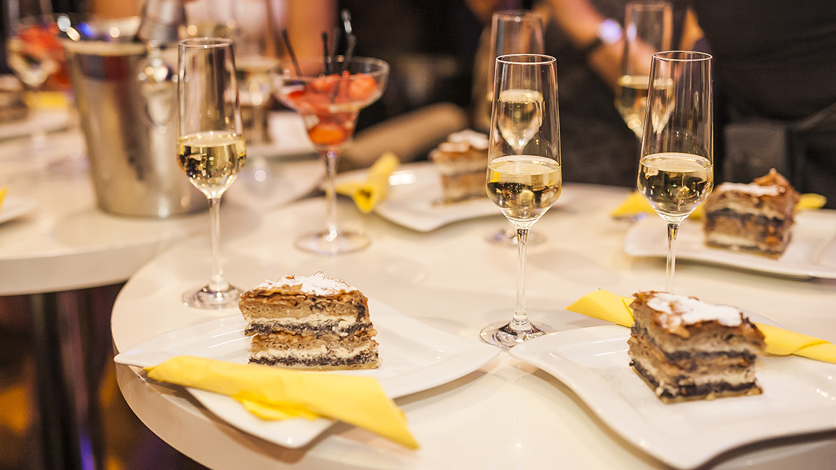 Une tranche de Prekmurska gibanica dans une assiette, accompagnée d'un verre de vin blanc.