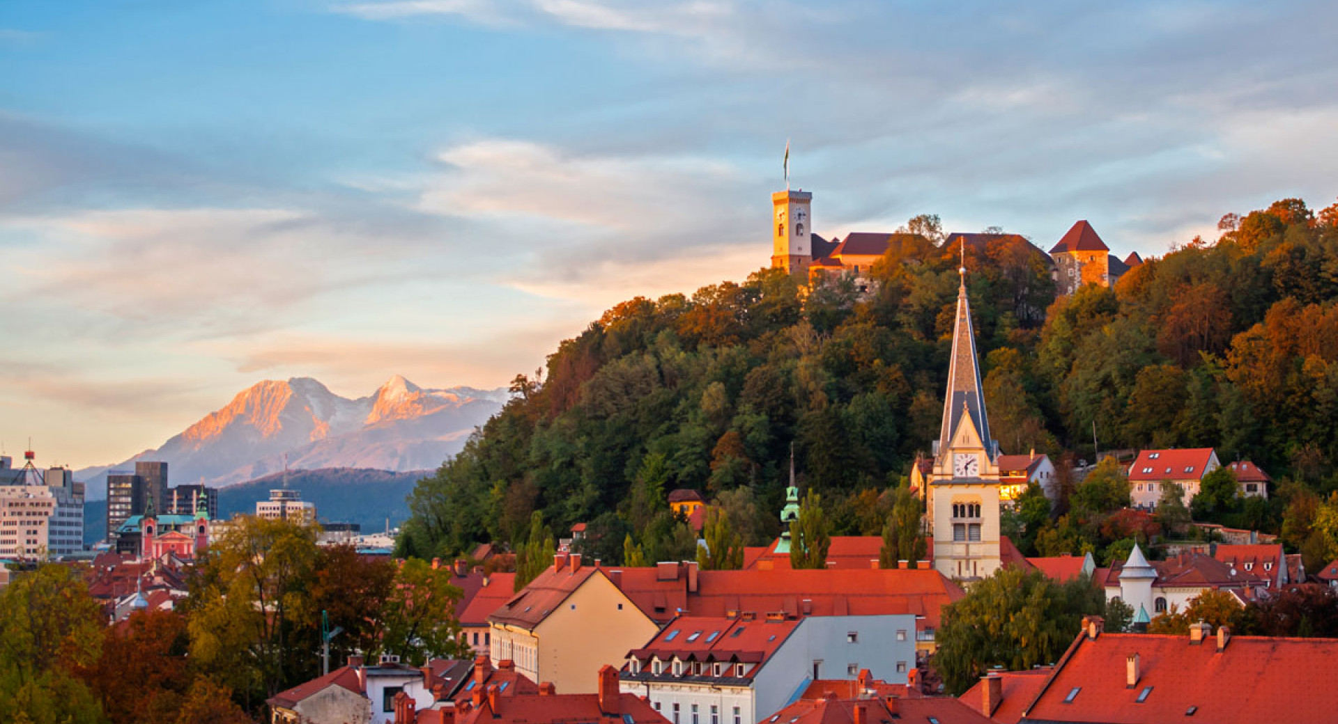 Ljubljanski grad nad strehami ljubljanskih hiš. V ozadju Alpe.