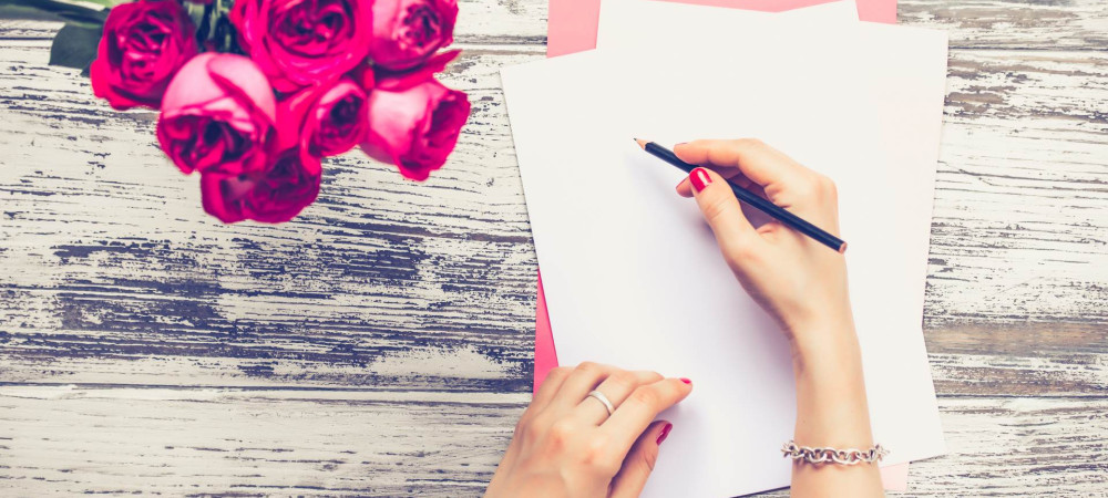 Roki ženske, v desni svinčnik, druga na listu papirja, zraven šopek rdečih vrtnic.