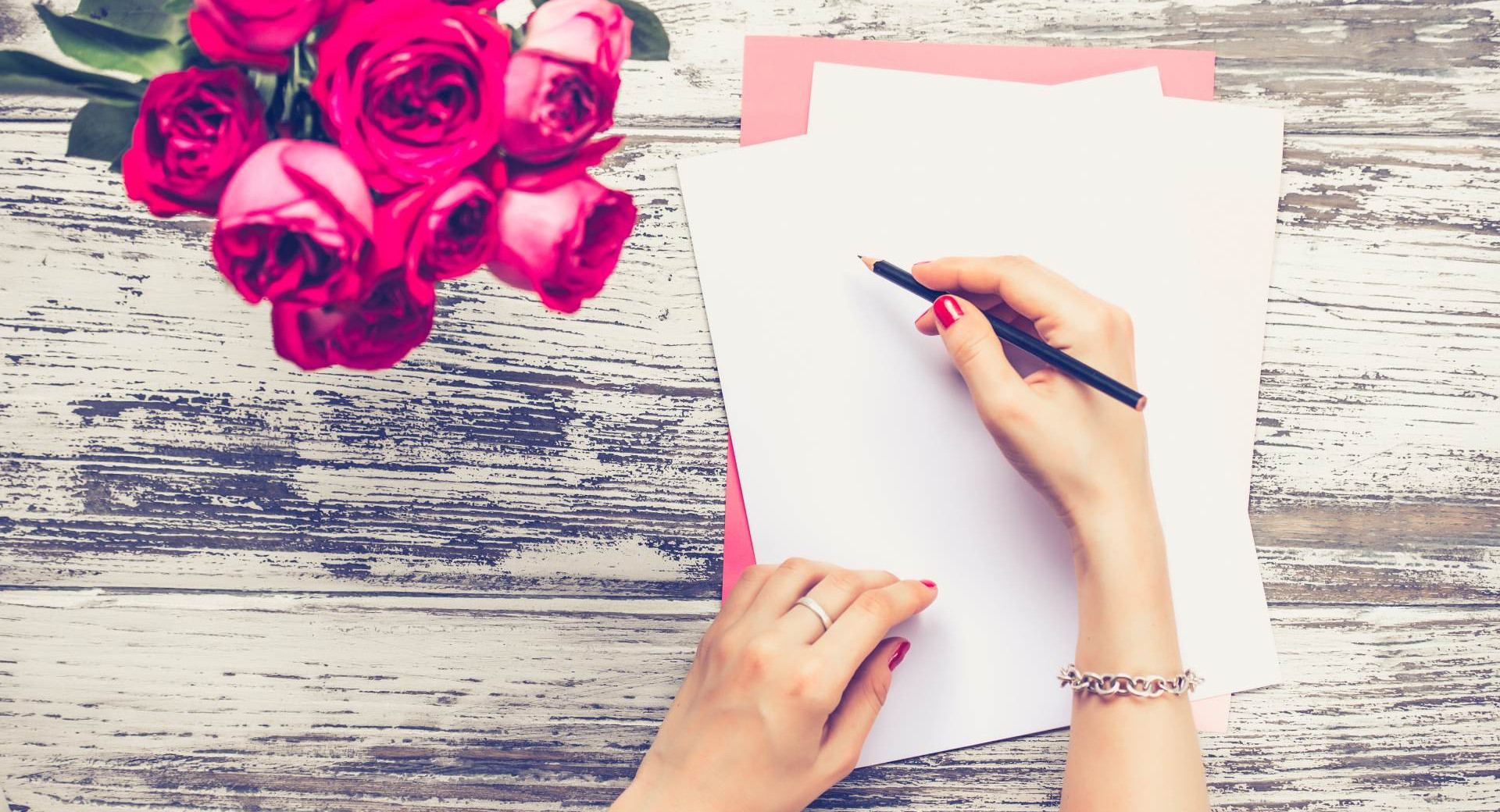 Roki ženske, v desni svinčnik, druga na listu papirja, zraven šopek rdečih vrtnic.