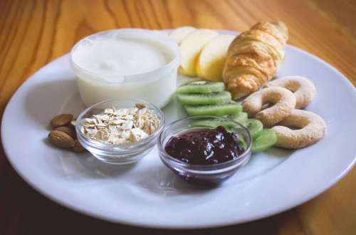 Zajtrk. Rogljiček, marmelada, jogurt in kosmiči na krožniku.