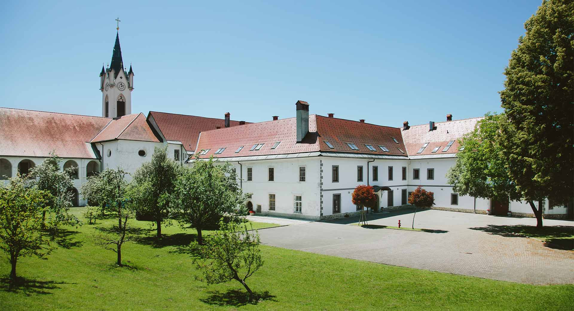 Zunanjost samostana z zvonikom in drevesi.