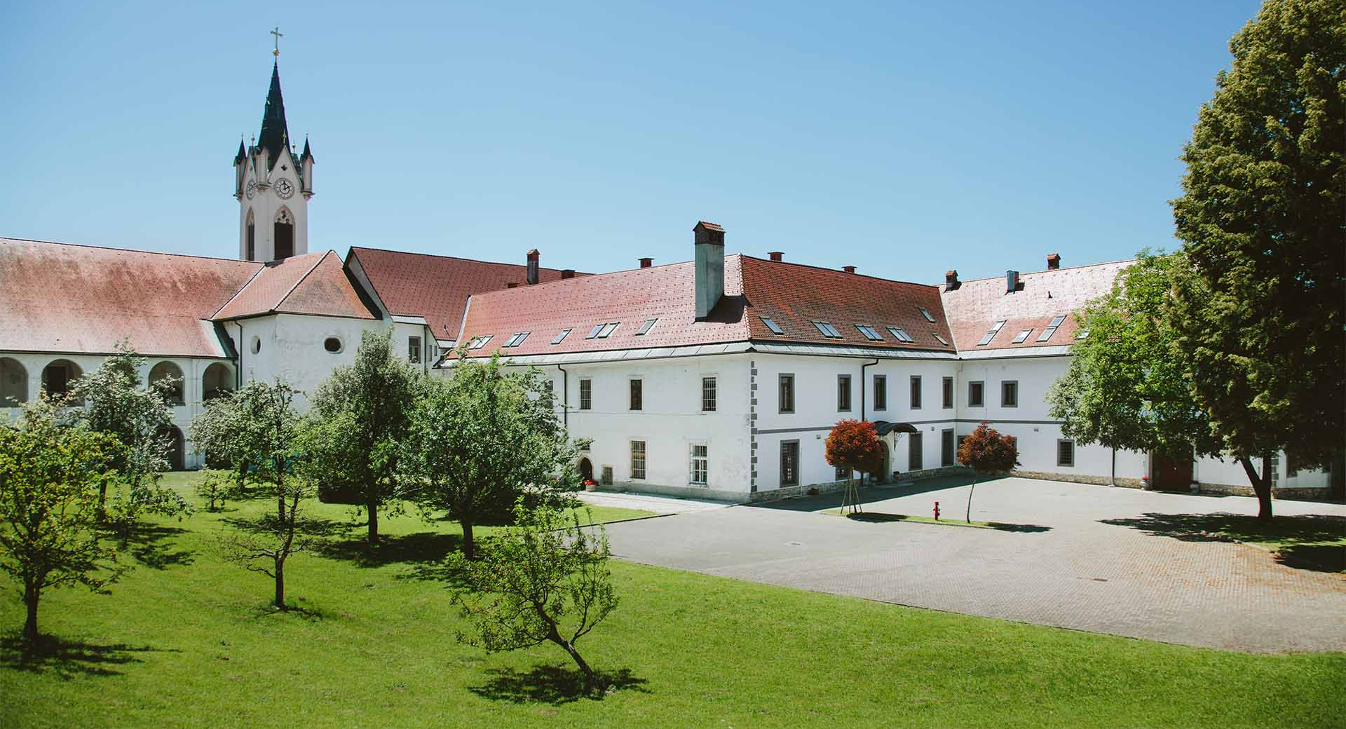 Zunanjost samostana z zvonikom in drevesi.