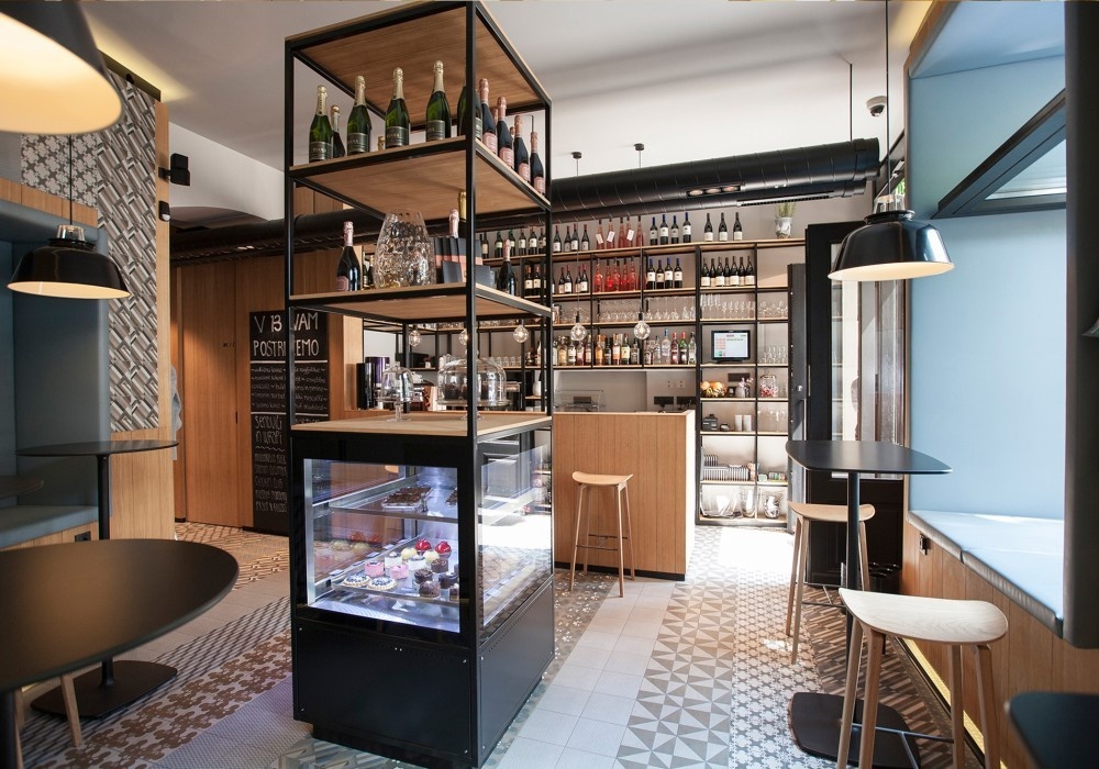 The interior of a café. A display of wine bottles and pastries.
