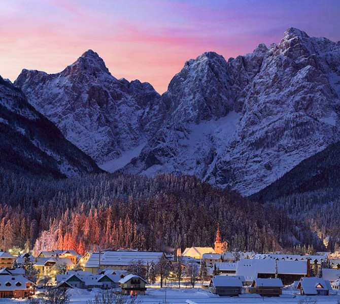 Kranjska Gora le soir sous la neige, avec des montagnes enneigées en arrière-plan.