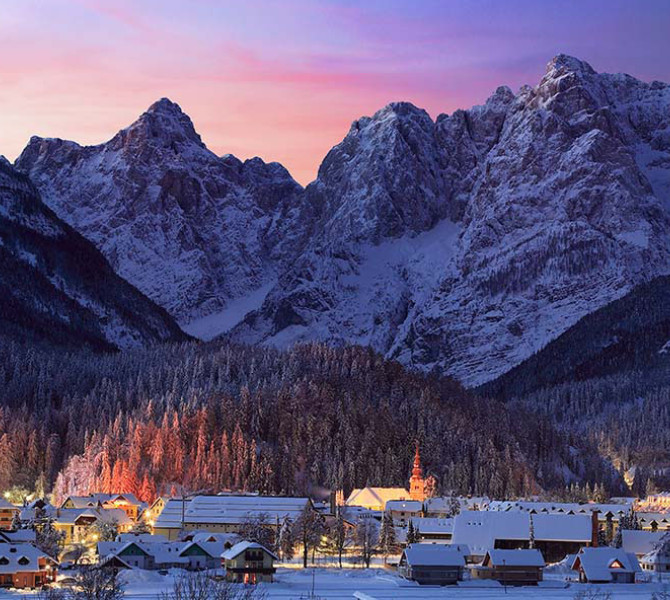 Kranjska Gora zvečer v snegu. V ozadju gore pokrite s snegom.
