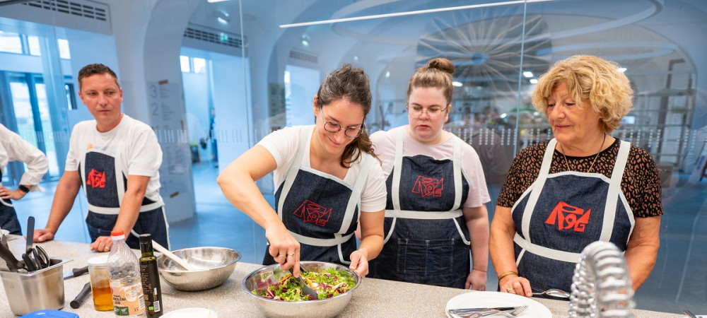 Un uomo e tre donne con grembiuli neri stanno preparando del cibo intorno a un tavolo.