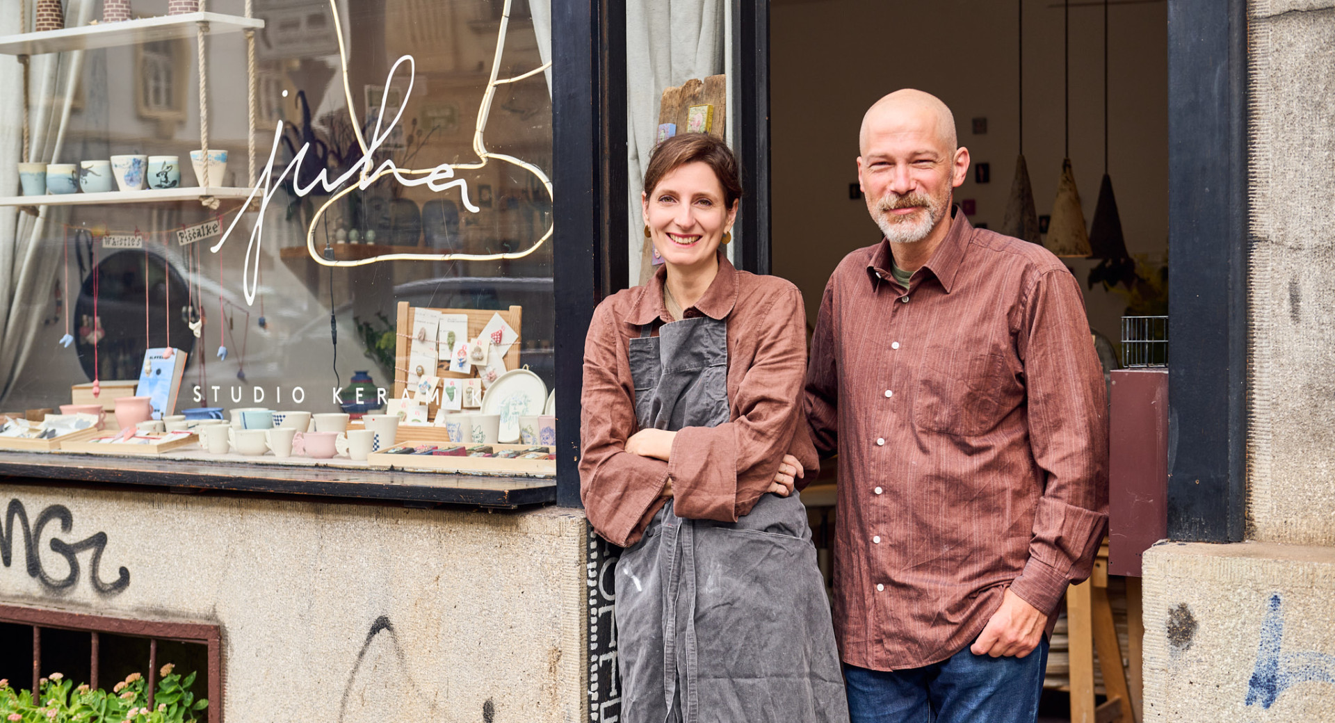  Dve osebi stojita pred vrati, ob izložbi s keramičnimi izdelki.