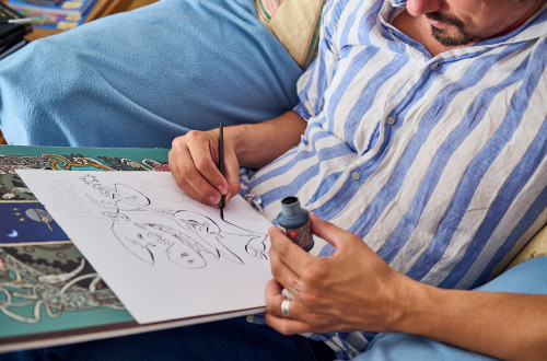 Moski v modro-beli crtasti srajci sedi in s crnilom rise risbo na papir.