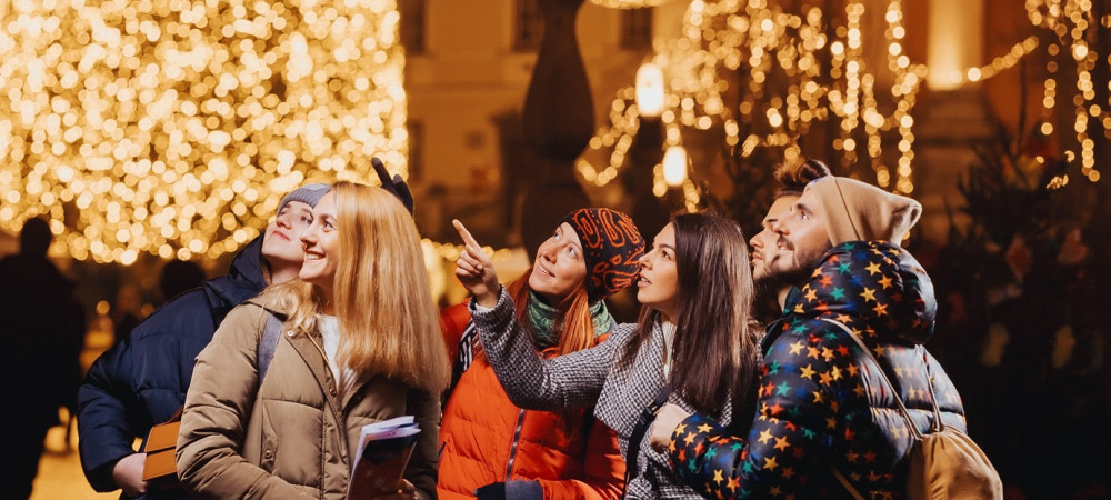 A group of young people dressed warmly looks up with interest, with a festive tree decorated behind them.