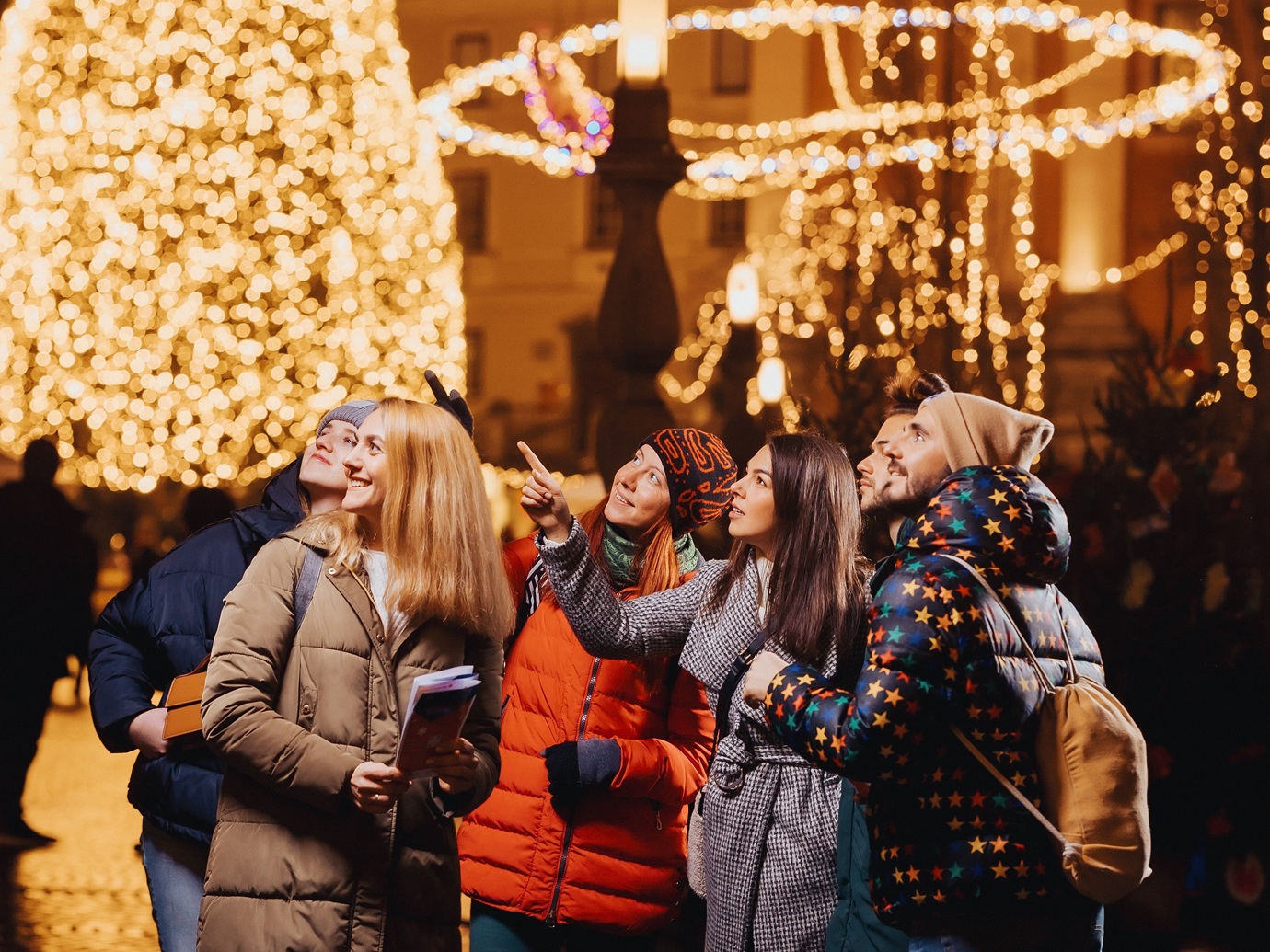 Un groupe de jeunes bien couverts regarde en haut avec intérêt, avec un arbre décoré de façon festive derrière eux.