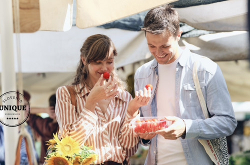 A smiling couple at the market is looking at and smelling cherry tomatoes.