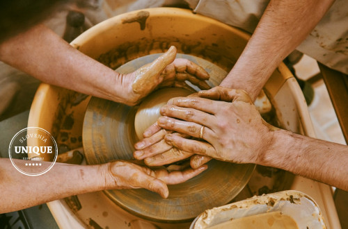Two pairs of hands are shaping a clay cup.