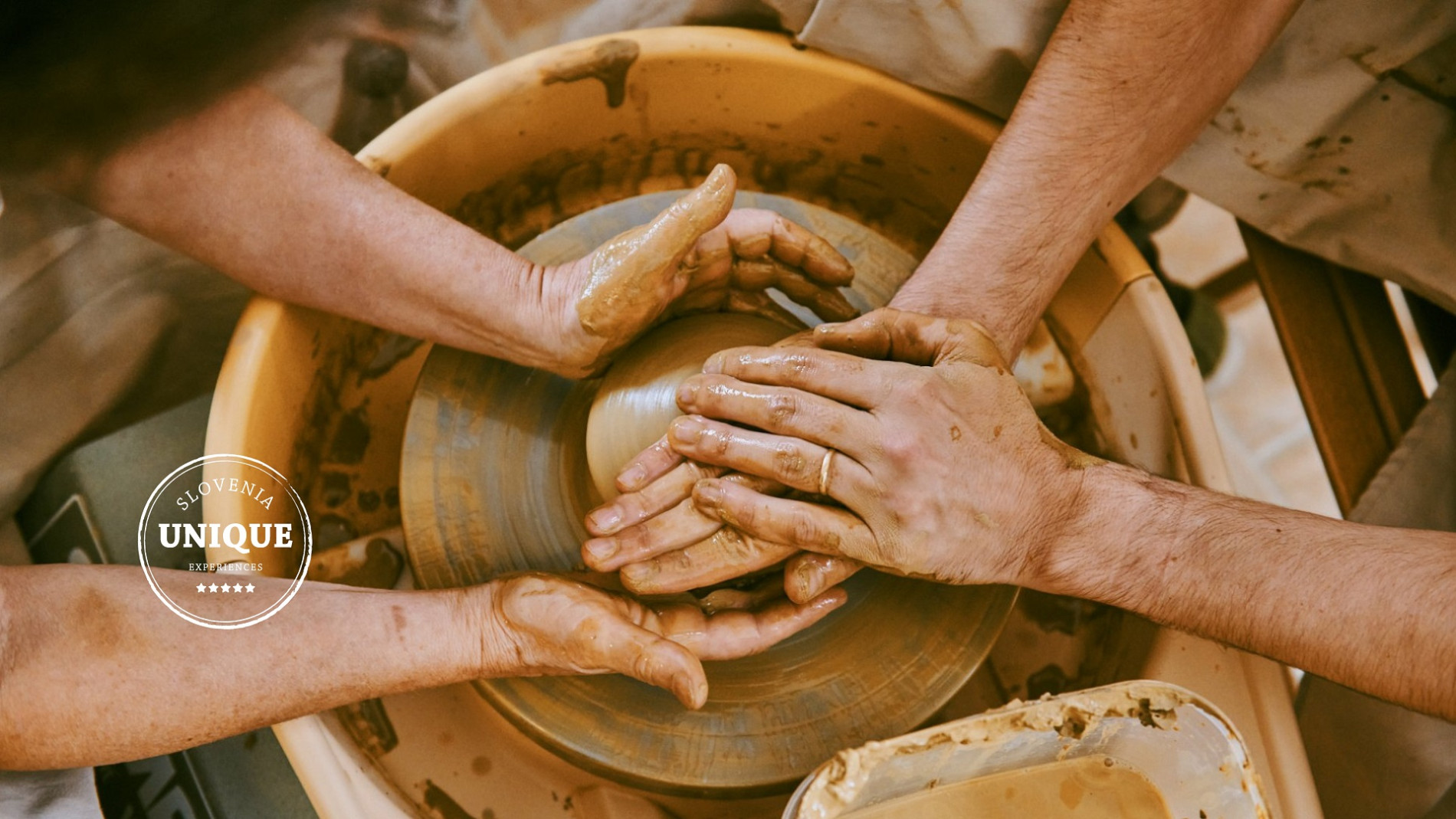 Two pairs of hands are shaping a clay cup.