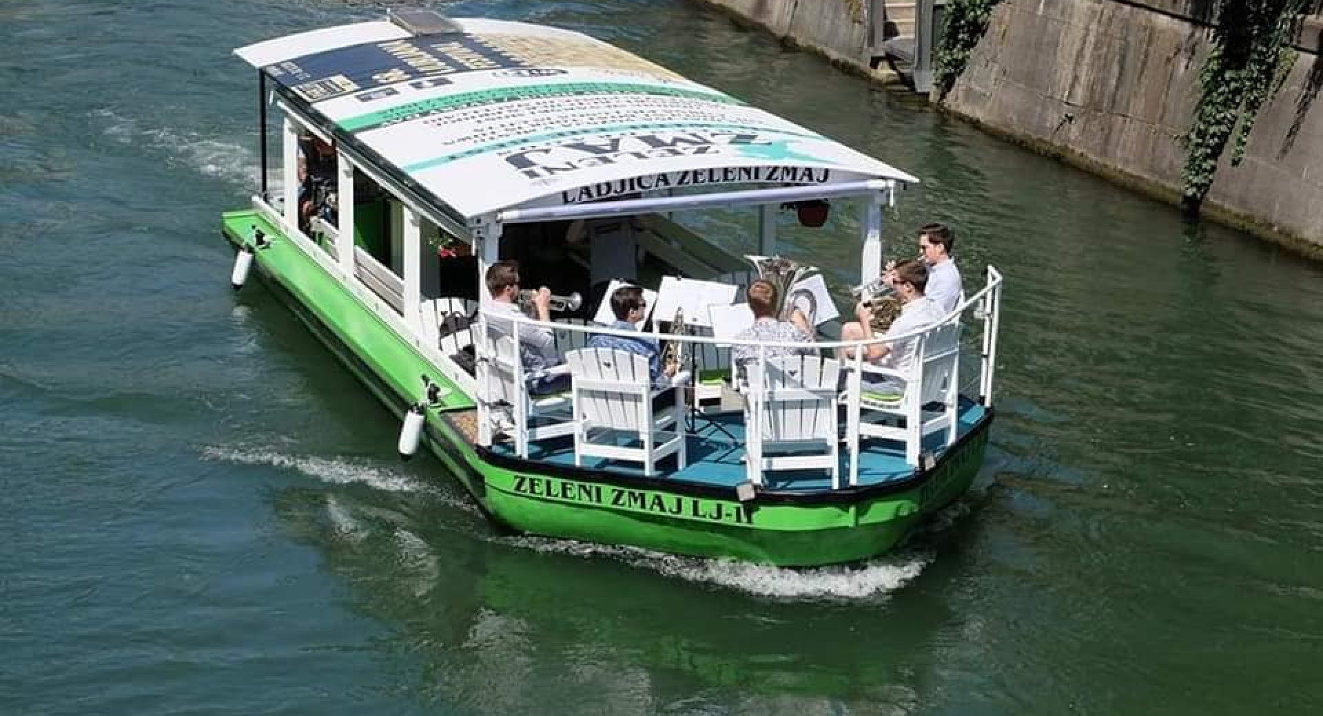 A bird’s-eye view of a boat on the Ljubljanica River, carrying a group of brass band musicians.